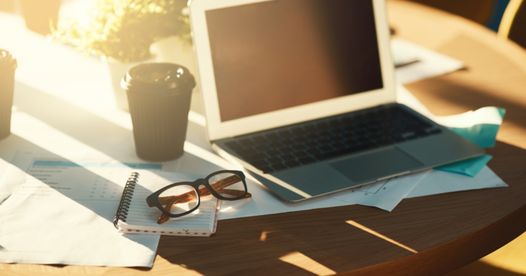 Desk with laptop, glasses, and papers in warm afternoon light — the weight of a workday.